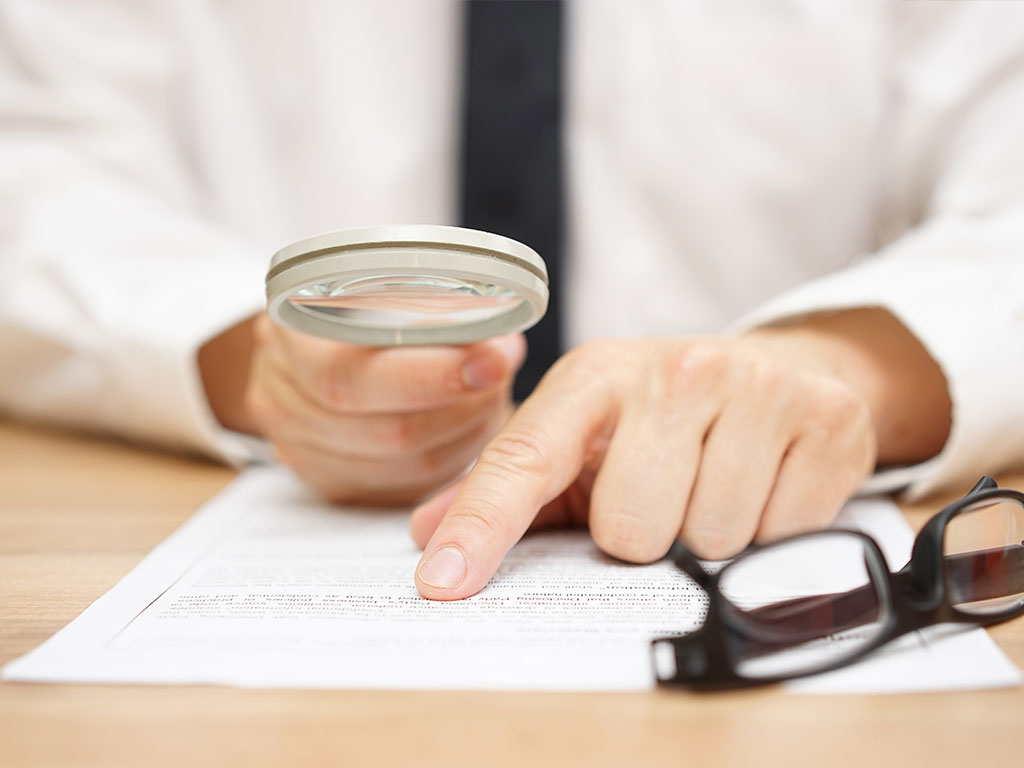 Man examining paperwork with a magnifying glass